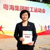 粤海集团工会副主席王敏女士的照片，她身着职业装站在公司职工运动会背景板前，手持赛事手册